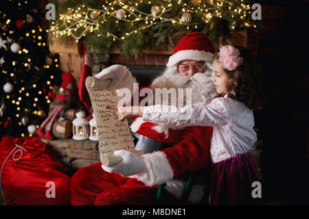 Ragazza giovane visitare Santa, puntando alla lista Foto Stock