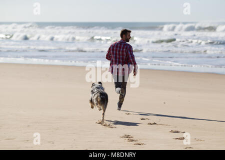 Running Man con il cane sulla spiaggia Foto Stock