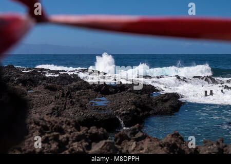 Nastro rosso attraverso le rocce per impedire alla gente di andare alla spiaggia dove ci sono molto mare mosso la rottura su rocce e rockpools sulla costa a un Foto Stock