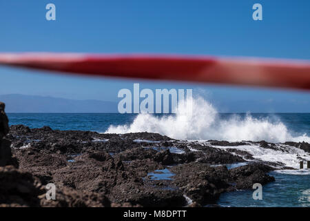 Nastro rosso attraverso le rocce per impedire alla gente di andare alla spiaggia dove ci sono molto mare mosso la rottura su rocce e rockpools sulla costa a un Foto Stock