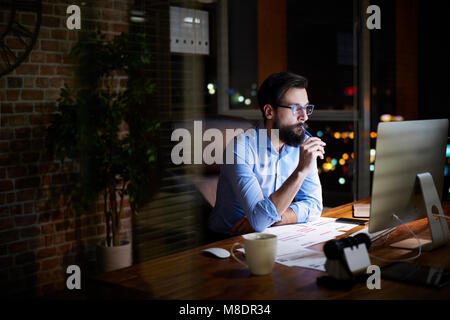 Giovane imprenditore guardare il computer sulla scrivania in ufficio durante la notte Foto Stock