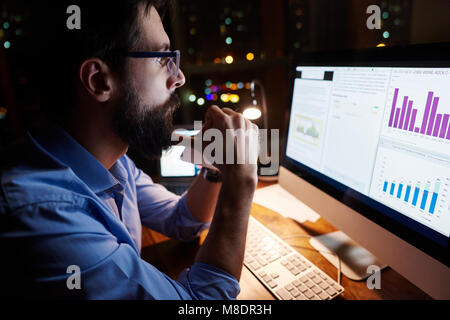 Giovane imprenditore guardare il computer sulla scrivania in ufficio durante la notte Foto Stock