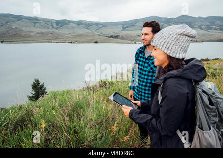 Escursionismo coppia, in piedi accanto al serbatoio di Dillon, giovane donna azienda digitale compressa, Silverthorne, Colorado, STATI UNITI D'AMERICA Foto Stock