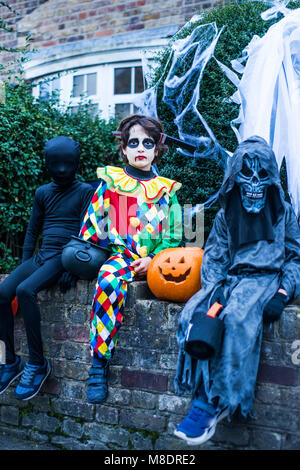 Ritratto di tre ragazzi in costumi di halloween, seduto sulla parete Foto Stock