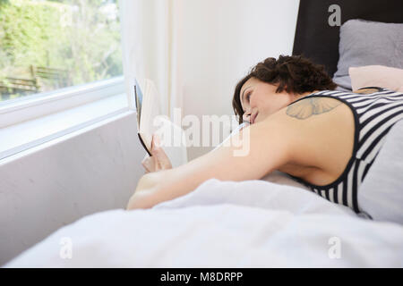 Metà donna adulta, rilassante sul letto, libro di lettura Foto Stock