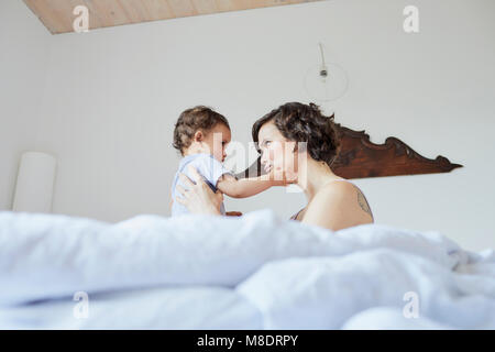 Madre seduta nel letto con Baby girl, faccia a faccia, pensieroso expression Foto Stock