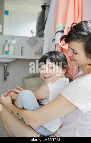 Madre e figlia insieme seduta in bagno, sorridente Foto Stock