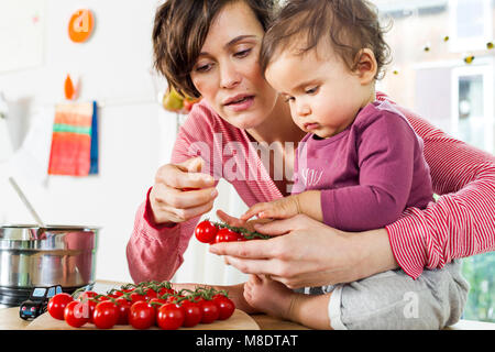 Il bambino e la madre figlia in cucina, ordinamento di pomodori sul banco di cucina Foto Stock