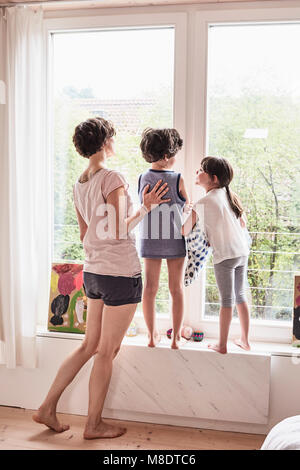 La madre e il figlio e la figlia a casa, guardando fuori della finestra, vista posteriore Foto Stock