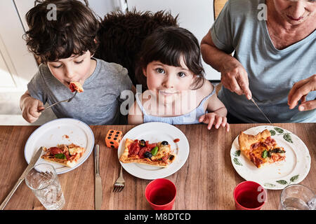 La nonna seduta al tavolo della cucina con i nipoti, mangiare la pizza, vista in elevazione Foto Stock