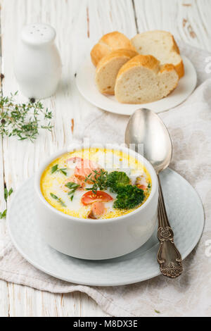 Salmone zuppa cremosa con verdure - patate, carote, pomodori e broccoli in una ciotola bianco luminoso su un tavolo di legno Foto Stock