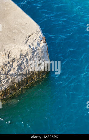 Molo di cemento grigio all'acqua di mare blu con piccole onde sotto la luce del sole brillante il giorno d'estate nel Porto Foto Stock