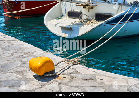 Motoscafo bianco lucido di design moderno ormeggiato al molo con corde sull'acqua di mare blu che riflette la luce del sole luminoso il giorno d'estate Foto Stock