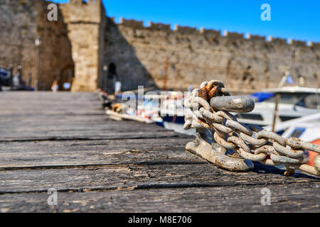 Ormeggio in metallo bitt con corda e catena su molo di legno a mare blu sotto la luce del sole brillante in estate giorno vista ravvicinata Foto Stock