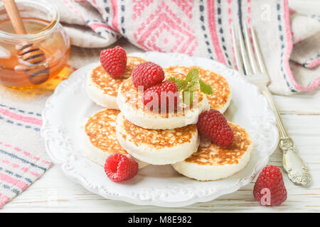 Formaggio di casa frittelle con miele e lamponi freschi. Syrniki. Tradizionale gustosa e sana prima colazione. Messa a fuoco selettiva Foto Stock