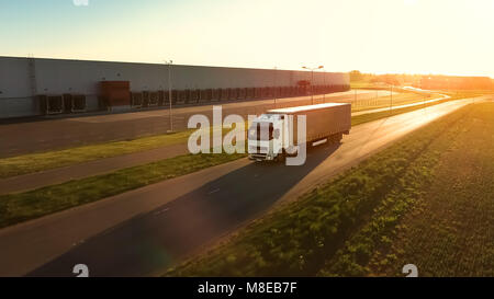 Vista aerea del White Semi camion con rimorchio carico muovendosi sull'autostrada. Sullo sfondo i magazzini e Area Rurale, Sun è l'impostazione. Foto Stock