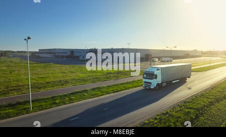 Riprese aeree del carrello bianco con semi rimorchio attaccato mobile attraverso il capannone industriale in area rurale. Il tramonto. Foto Stock