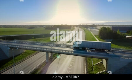 Riprese aeree del carrello bianco con semi rimorchio spostando su autostrada. Sullo sfondo i magazzini e Area Rurale, Sun è l'impostazione. Foto Stock