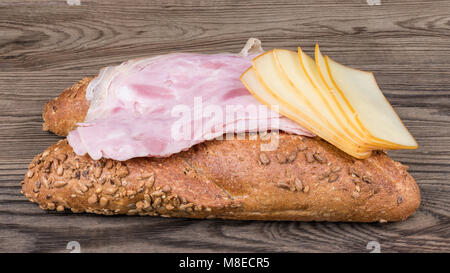 Due lunghi rotoli di pane con fette di prosciutto hock e formaggi stagionati. Croccante di grano intero baguette con fette di prosciutto affumicato e formaggio edam su uno sfondo di legno. Foto Stock