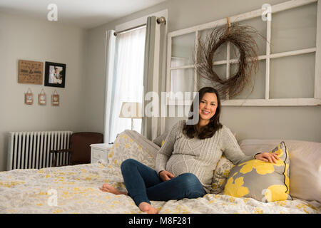 Donna incinta seduta sul letto Foto Stock