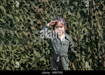 Ragazza asiatica rispetto soldato con azione soldato verde o pilota uniforme su una texture verde net sfondo bunker Foto Stock