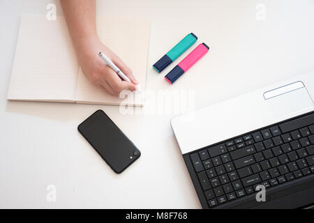 Compiti di scrittura sulla scrivania accanto al portatile e telefono Foto Stock