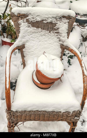 Sedia di vimini ricoperto di neve e un vaso di fiori riempito di neve sul sedile Foto Stock