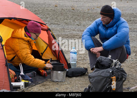 L'alpinista giovane la cottura dei cibi e tè presso una base remota camp nel selvaggio Cordillera Blanca nelle Ande del Perù durante una escursione di alpinismo Foto Stock