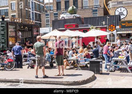 Pop up ristoranti esterni bancarelle con persone mangiare su tavoli outiside presso la Old Truman Brewery, Ely's Yard, Shoreditch, London, Regno Unito Foto Stock