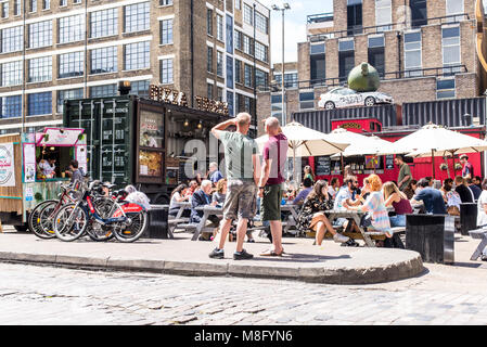 Pop up ristoranti esterni bancarelle con persone mangiare su tavoli outiside presso la Old Truman Brewery, Ely's Yard, Shoreditch, London, Regno Unito Foto Stock