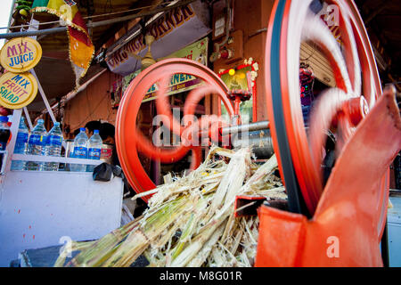 Una immagine di un arancione macchina di canna da zucchero in movimento spremendo il succo di canna da zucchero. La foto viene scattata alla strada del mercato di Jodhpur India. Le ruote Foto Stock
