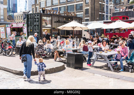 Pop up ristoranti esterni bancarelle con persone mangiare su tavoli outiside presso la Old Truman Brewery, Ely's Yard, Shoreditch, London, Regno Unito Foto Stock