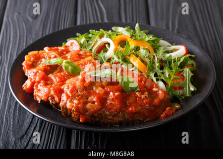 Il cibo italiano: Carne alla pizzaiola e insalata fresca closeup su una piastra sul tavolo orizzontale. Foto Stock