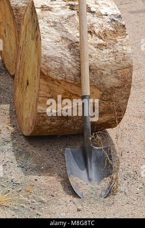 La pala con un manico in legno appoggiata contro un log di sabbia sul terreno. Foto Stock