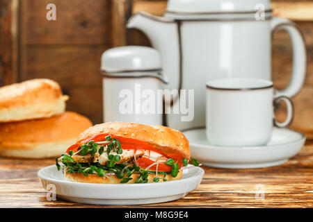 Semi di sesamo grano intero bagel con chicken grill, Microgreens, cetriolo e avocado su piastra bianca su sfondo grigio. Colazione sana nozione . S Foto Stock