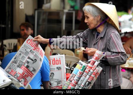 Hanoi, Vietnam - Marzo 15, 2018: Senior lady vendita di quotidiani locali con una bicicletta Foto Stock