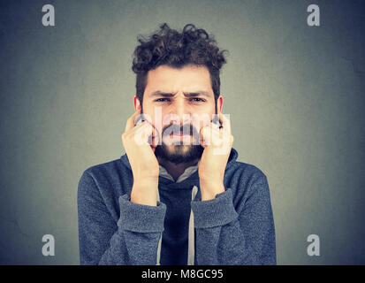 Infastiditi man looking grumpy tamponamento con le dita le orecchie disposta ad ascoltare chiunque. Foto Stock