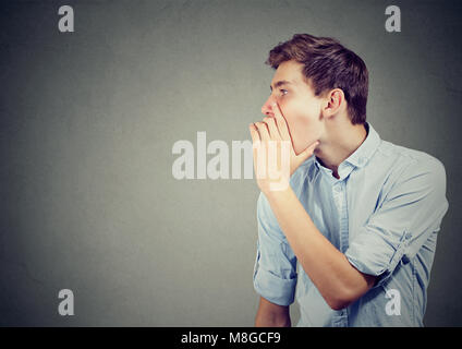 Giovane uomo che copre la bocca mentre spettegolare e raccontare segreti in sussurro. Foto Stock