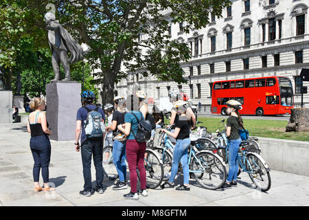 Gruppo di turisti in bicicletta & tour guida con biciclette a noleggio persone intorno a statua del David Lloyd George in piazza del Parlamento red bus Londra Inghilterra REGNO UNITO Foto Stock