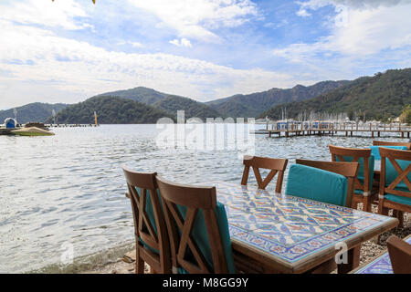 Tavolo con sedie a sdraio sulla spiaggia gocek con montagne a Gocek, Turchia Foto Stock