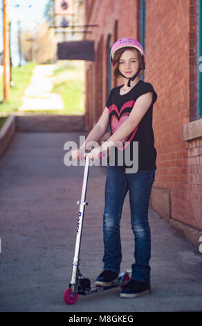 Preteen ragazza con i capelli rossi e le lentiggini, sul marciapiede con il suo alluminio kick scooter. Foto Stock