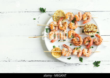 Grigliata di gamberi spiedini. Frutti di mare, shelfish. Gamberi spiedini con spezie e erbe aromatiche fresche in bianco sullo sfondo di legno, copia dello spazio. Gamberi b Foto Stock