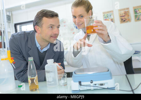 Tecnico di laboratorio miscelazione liquidi in laboratorio assistente durante la scrittura dei dati Foto Stock