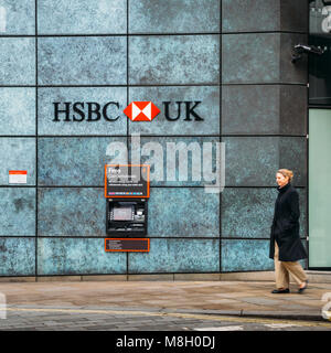 Londra, UK- Mar 13, 2018: donna di mezza età cammina passato un Bancomat dalla banca HSBC pubblicità il prelievo gratuito di denaro contante Foto Stock