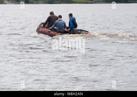Tre uomini non identificati in un mantello rosso, corre rossa gomma gonfiabile barca con motore fuoribordo sul lago blu foresta caduta in una giornata di sole Foto Stock