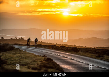 Due ciclisti su strada sulla strada passato Haytor su Dartmoor nel Devon a sunrise. Foto Stock