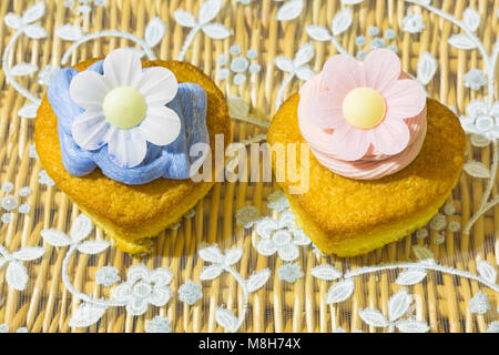 Home realizzata a forma di cuore ad cupcake torte, uno con Fragola Rosa la glassa glassa e uno con il blu e carta di riso commestibile fiore a margherita Foto Stock