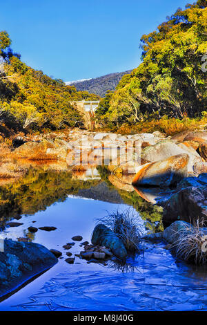 Coperte di ghiaccio fiume nevoso in montagne innevate dell Australia su una soleggiata giornata invernale con Snow capped picco di montagna su Guthega diga di Snowy idroelettrica Energia sc Foto Stock