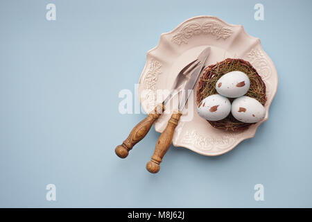 Vacanze di Pasqua scheda con messa in tavola con uova colorate pastello su sfondo blu Foto Stock