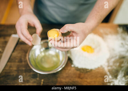 Pasta processo di cottura, maschio chef mani con uovo, un mazzetto di farina a fontana sul tavolo di legno Foto Stock